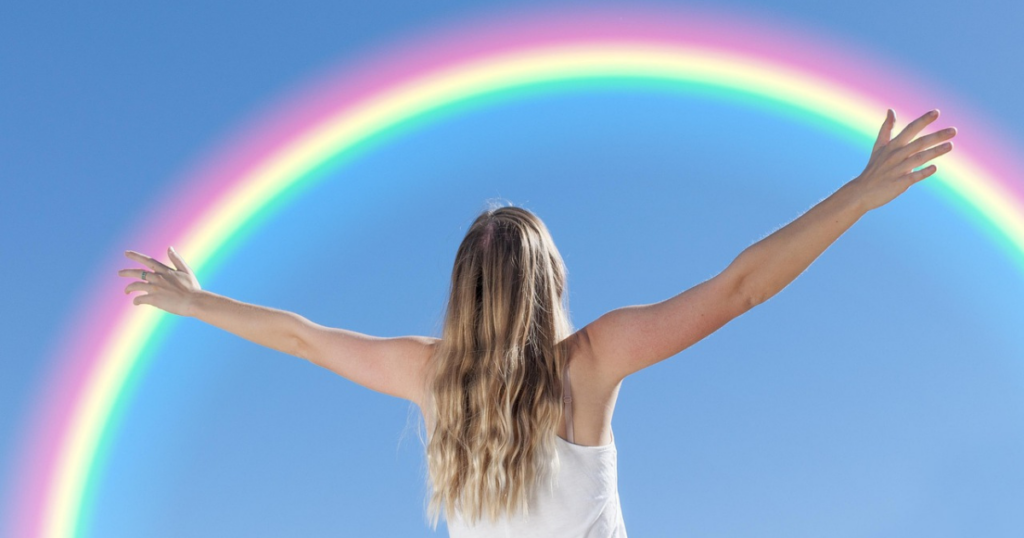 Femme de dos contemplant un arc-en-ciel, symbole de présence à soi et d’alignement intérieur.